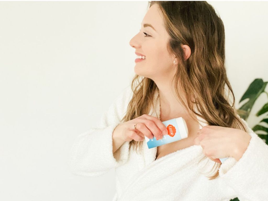 woman wearing white robe putting Lume deodorant on 