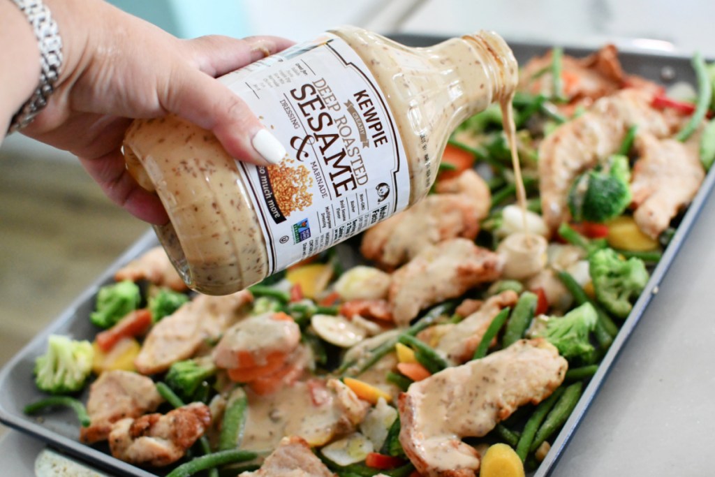 pouring kewpie dressing on the sheet pan veggies and chicken