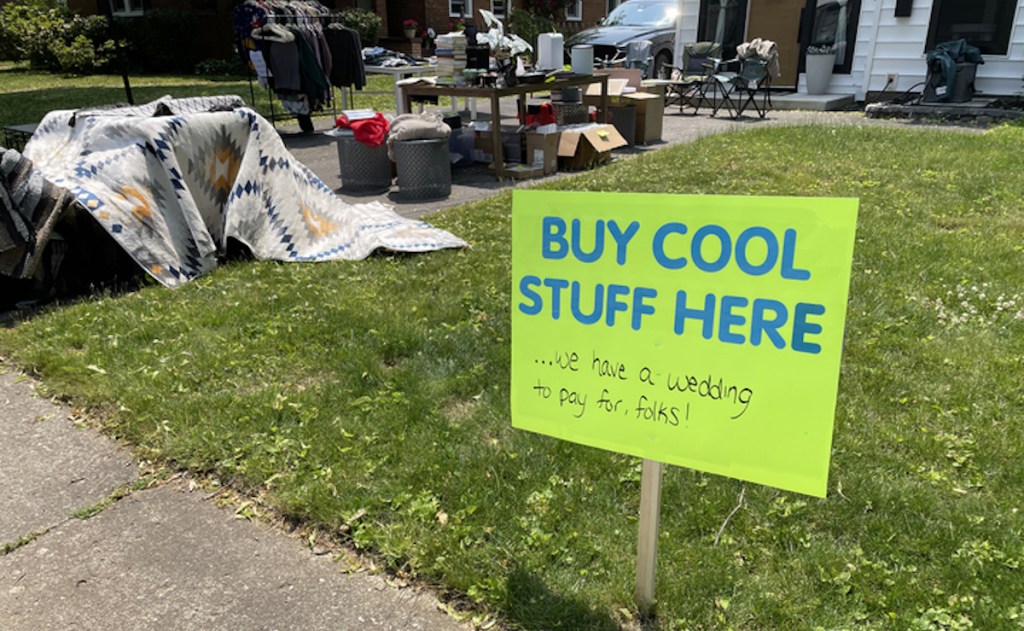 yard sale sign for wedding with stuff to buy in the background