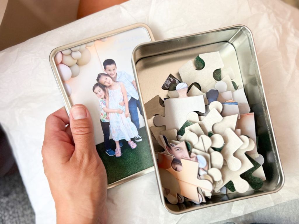 Walgreens Photo Puzzle pieces shown in the keepsake tin with a women's hand holding the lid