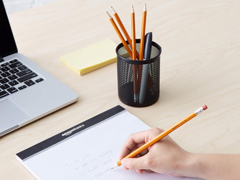 person writing on notepad with yellow pencil