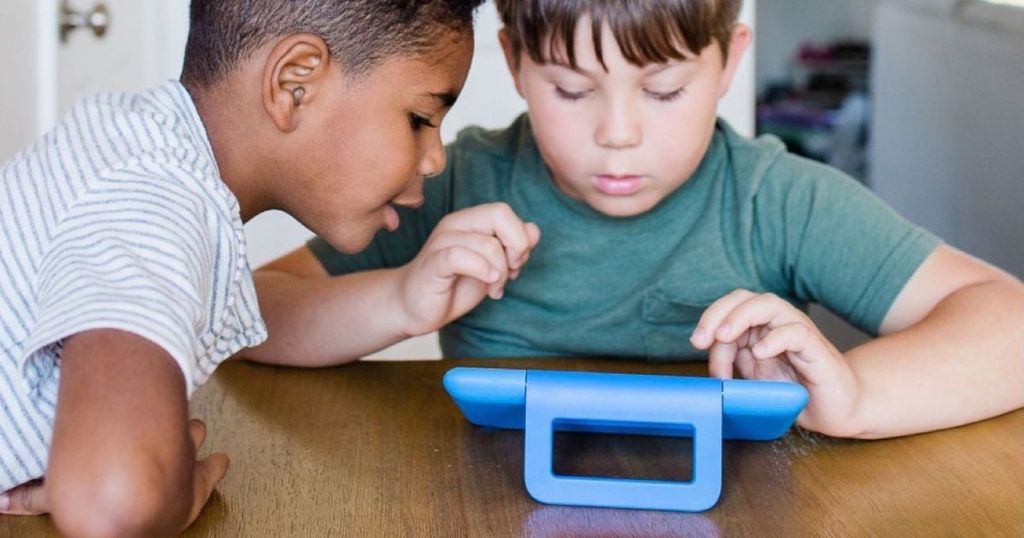 2 boys sitting at table looking at blue Amazon tablet