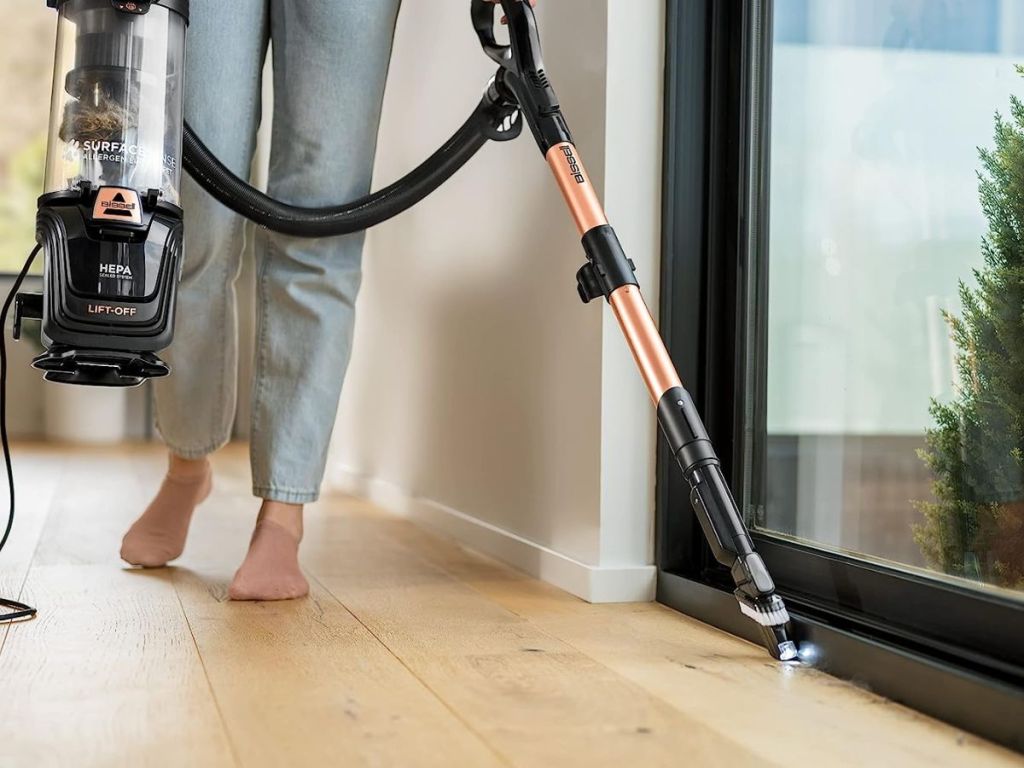 person holding vacuum wand cleaning near sliding glass door
