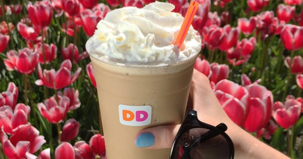 hand holding a dunkin frozen coffee and sunglasses with lots of flowers in the background