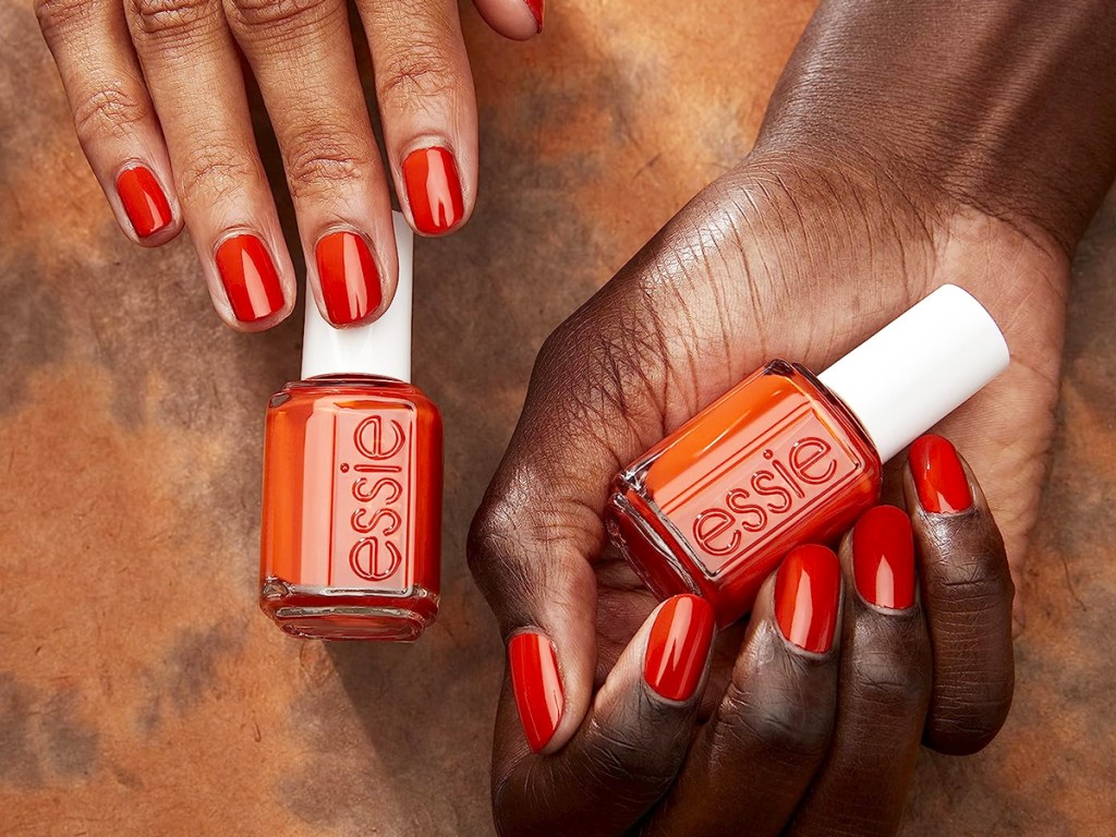 two hands holding bottles of orange essie nail polish