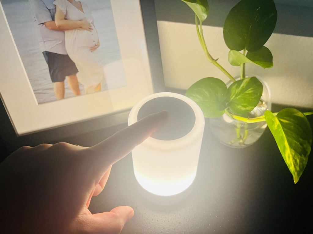 finger touching the top of a touch night light on dresser with photo frame and plant