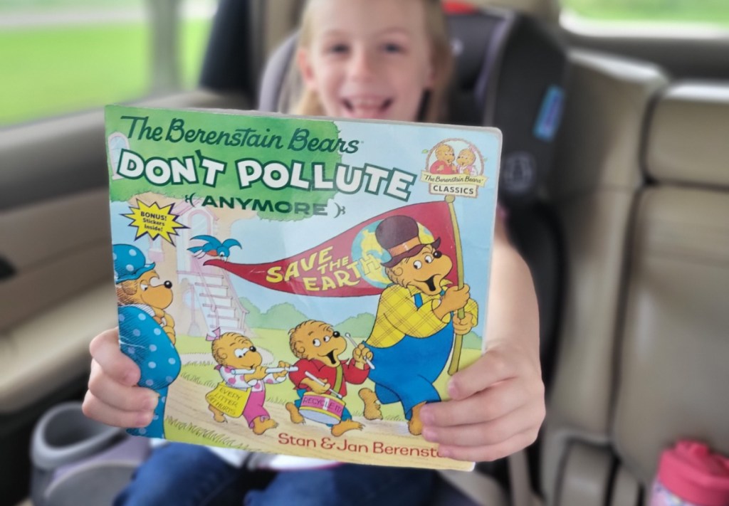 A young girl riding in a car and holding a FREE Berenstain Bears book she got from Kellogg's Feeding Reading Program