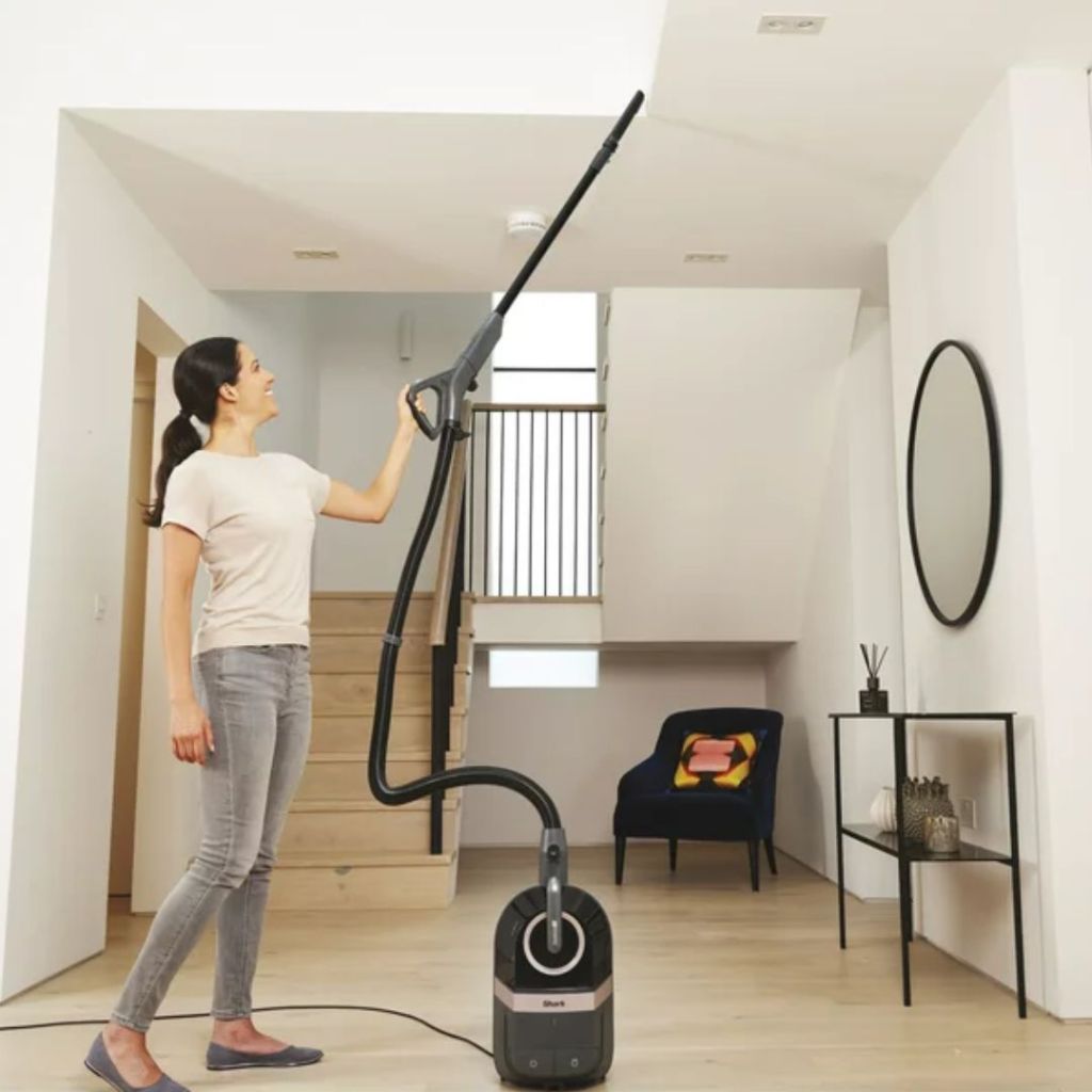 Woman vacuuming ceiling beams with a Shark Bagless Corded Canister Vacuum