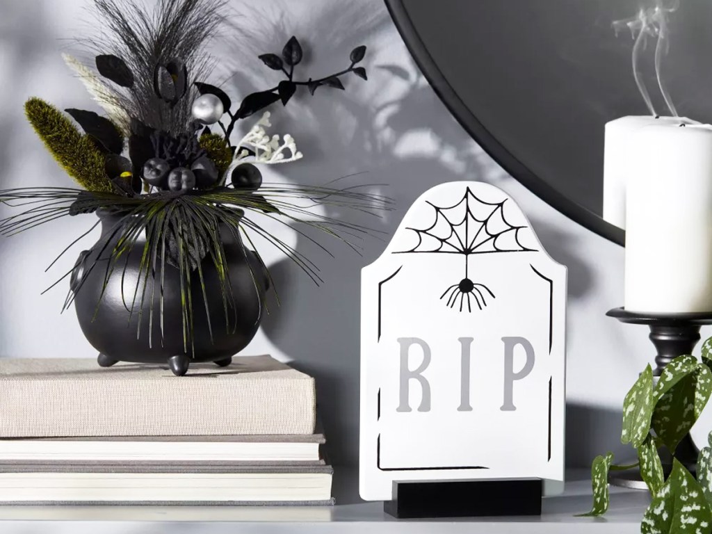 white rip tombstone on mantel next to black floral arrangement and candle