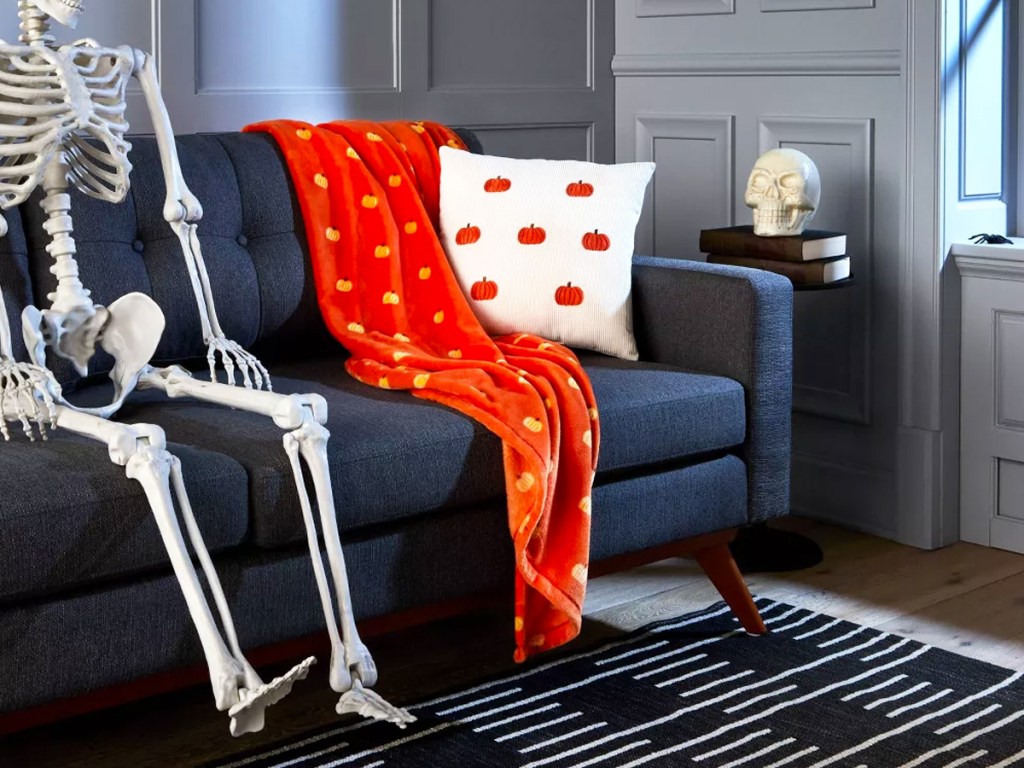 skeleton on couch next to halloween throw and pillow