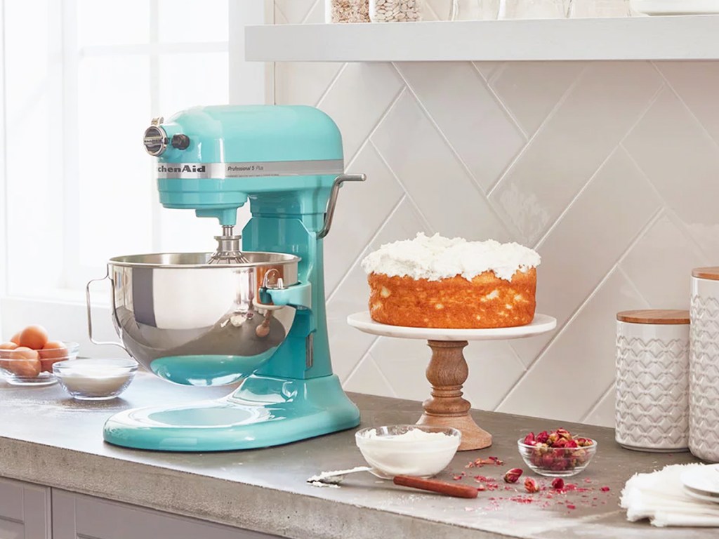 teal kitchenaid mixer on counter near cake and ingredients in bowls