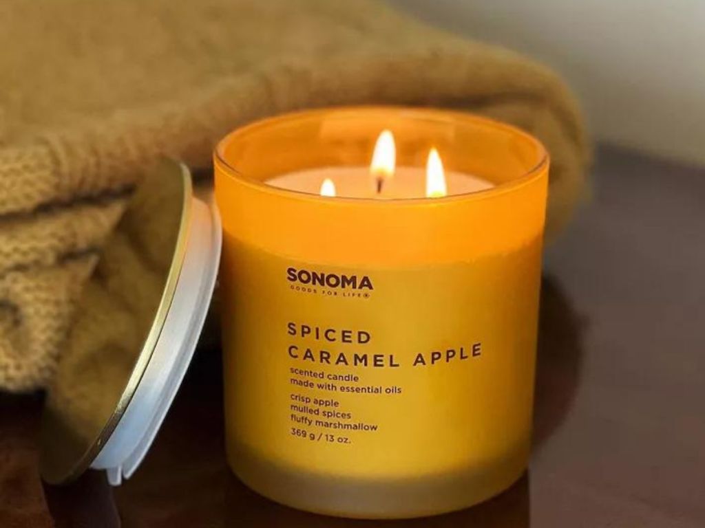 A lit Spiced Caramel Apple Candle by Sonoma Goods for Life set near a blanket 