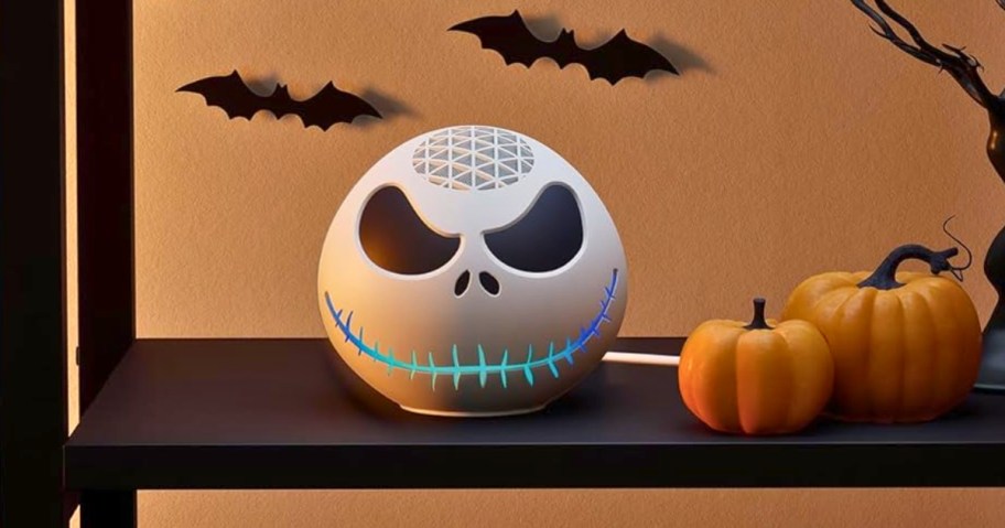 an Echo dot machine with a Jack Skellington from Nightmare Before Christmas cover sitting on a bookcase with Halloween decorative bats behind it and a faux pumpkins beside it