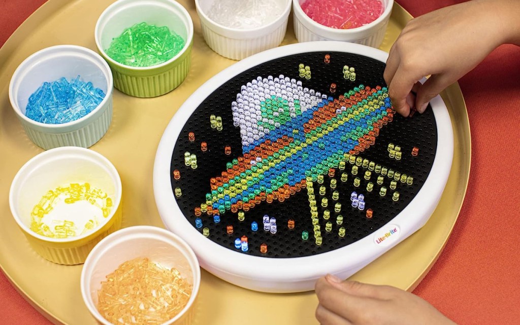 a child's hand placing lite brite pegs into an oval lite brite 
