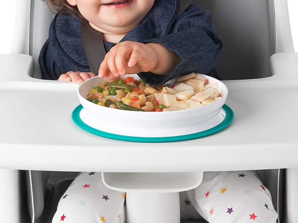 A toddler eating at a highchair with a plate of food