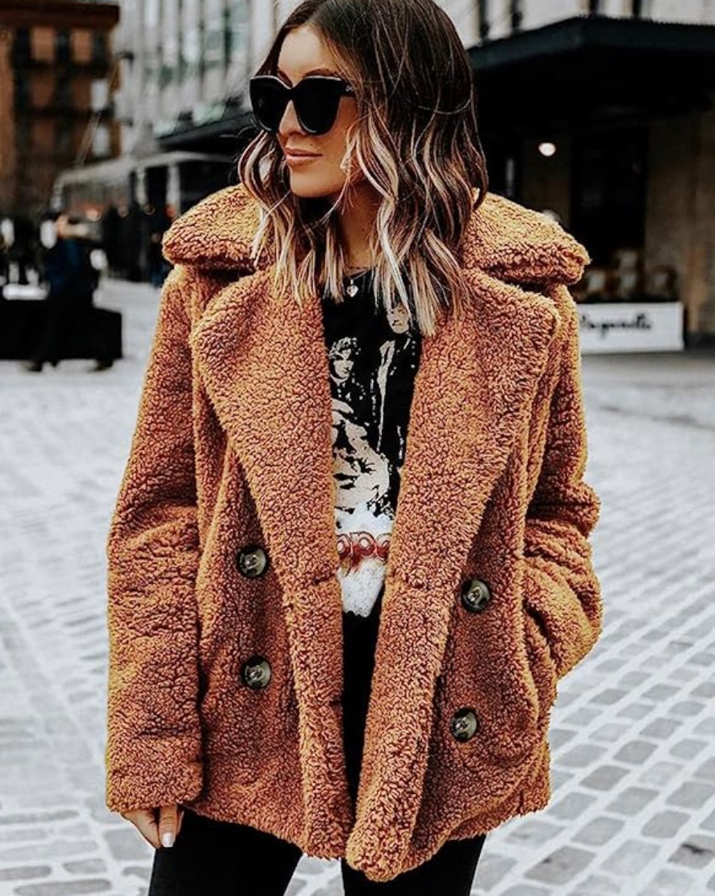 woman wearing brown sherpa jacket and oversized sunglasses in city street