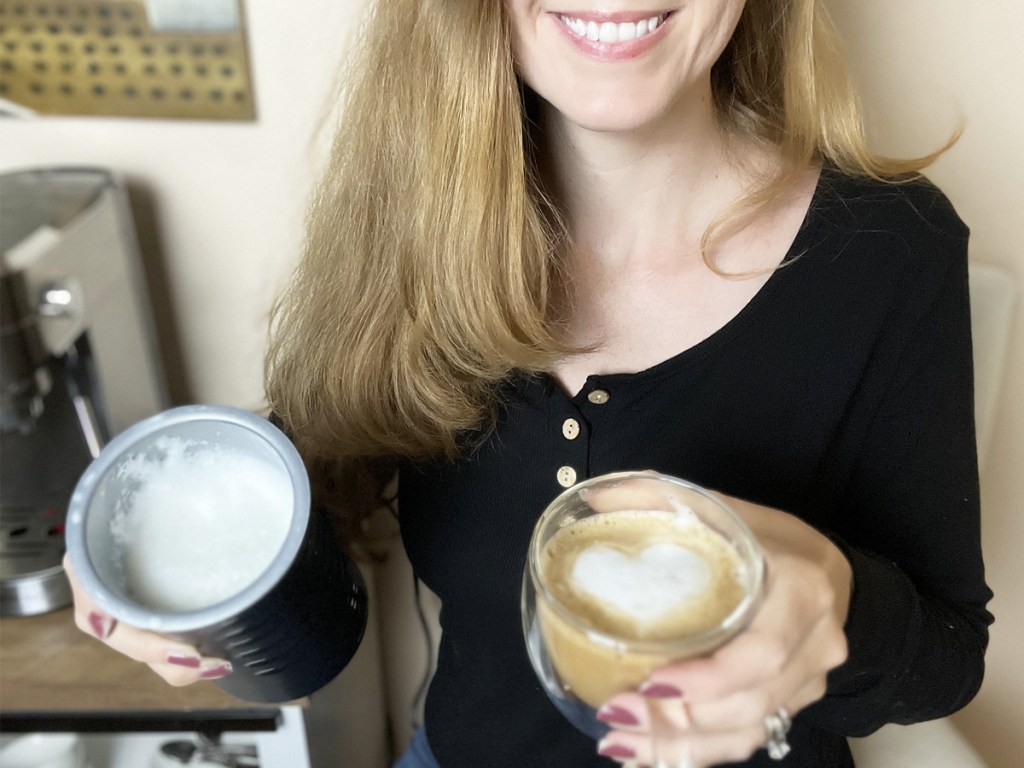 woman holding a milk frother and a latte with a foam heart