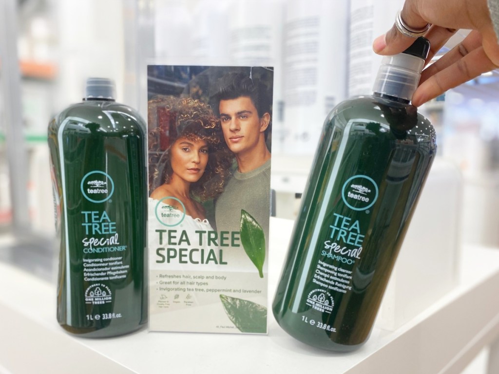 hand grabbing 1-liter bottles of Paul Mitchell Tea Tree shampoo and conditioner