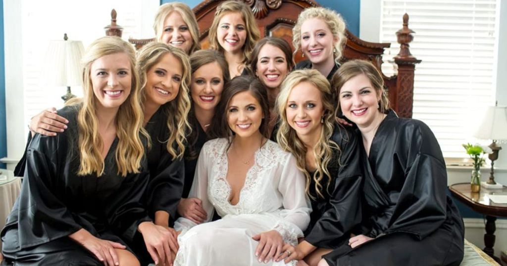 A group of bridesmaids in black robes and a bride in a white robe. 