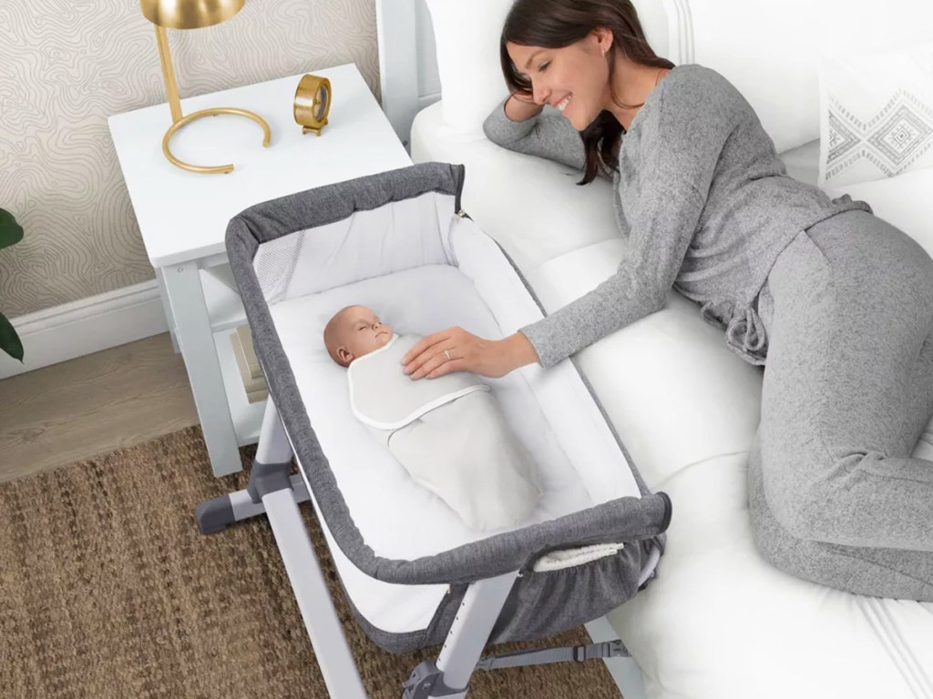 mom in bed touching baby in bassinet