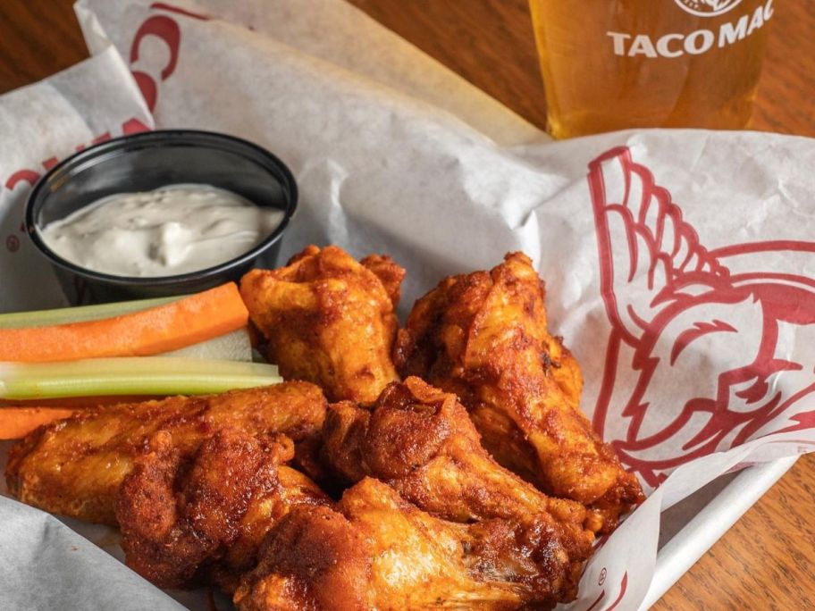 A basket of buffalo chicken wings with sauce in a basket next to a beer