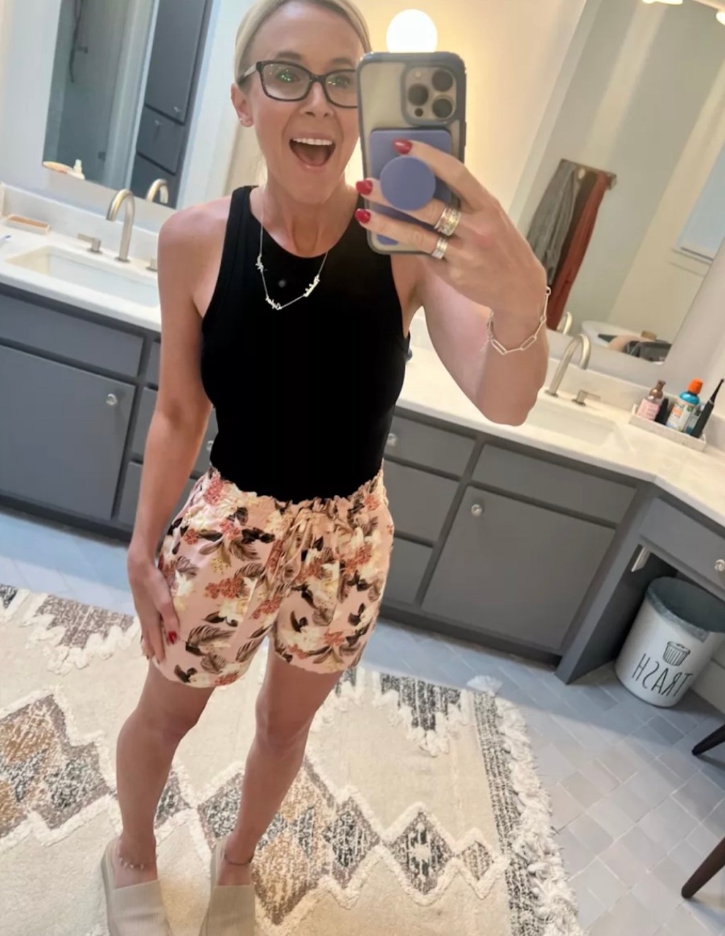 woman taking mirror selfie wearing black bodysuit and floral shorts in bathroom