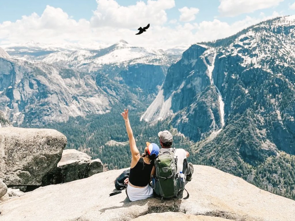 couple sitting on rock at yosemite with bird flying in sky