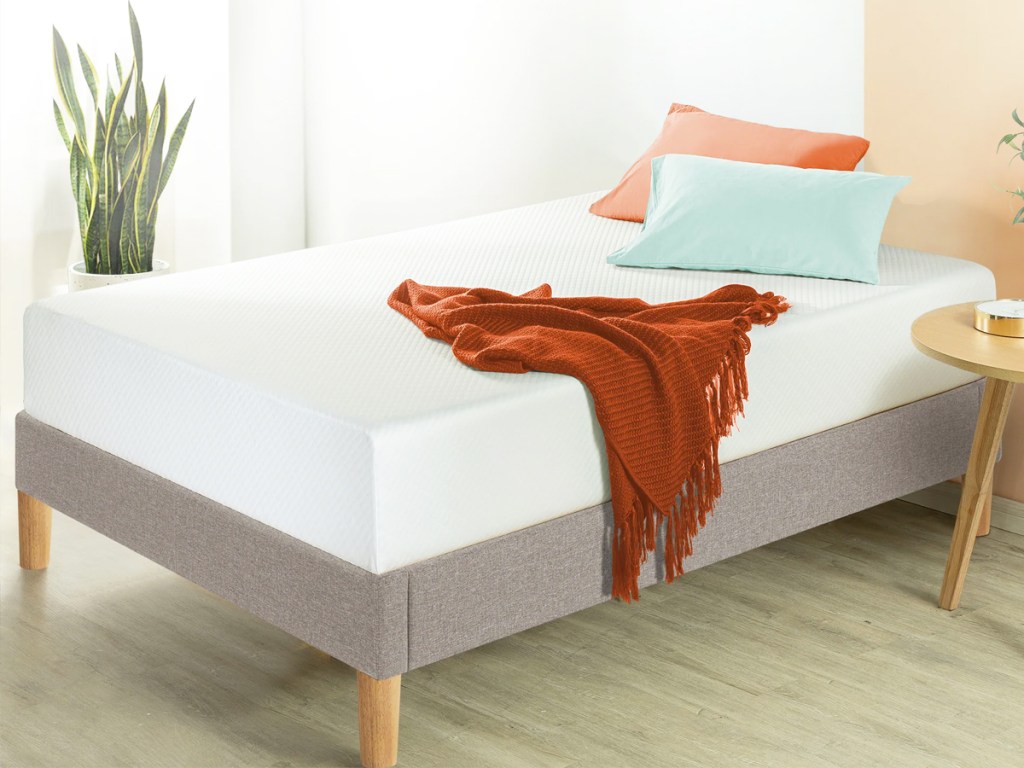 white mattress on a grey bed frame with pillows and throw on top