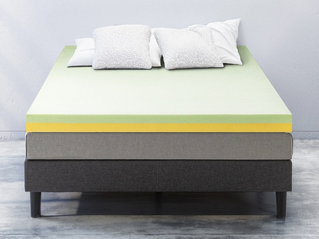 mattress with a green and yellow foam topper and pillows on top