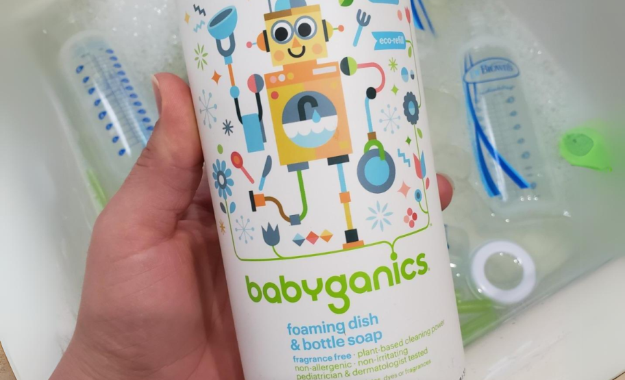 a womans hand holding a bottle of babyganics dish and bottle soap with a sink in the background