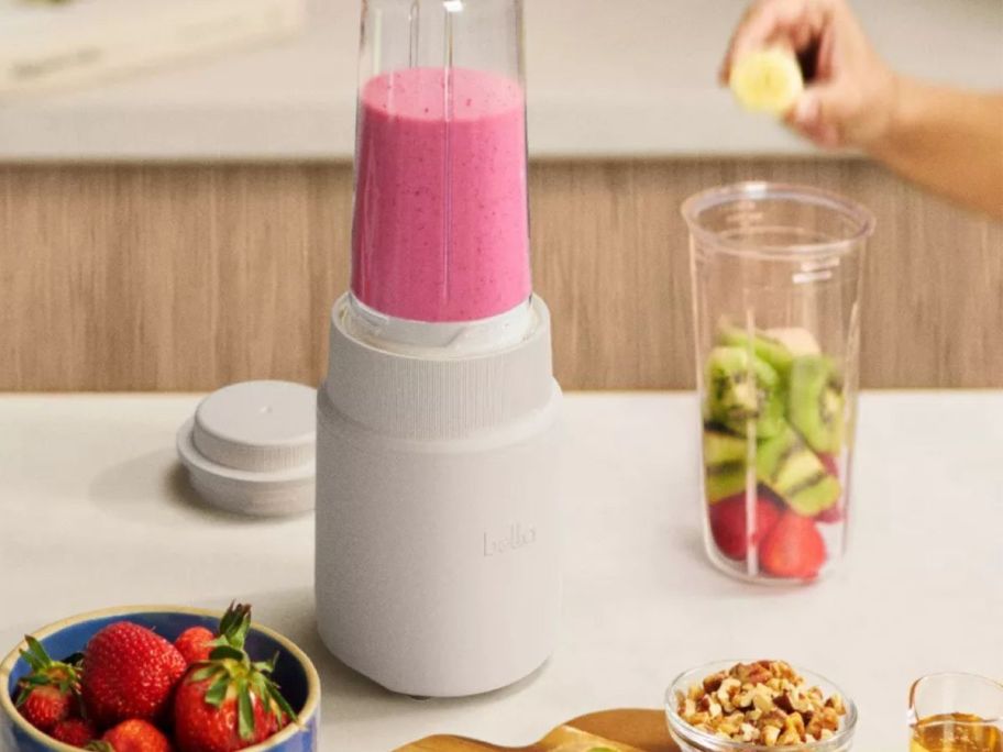 white Bella Portable Rocket Personal Blender with a smoothie blended in it and fruit around it on counter