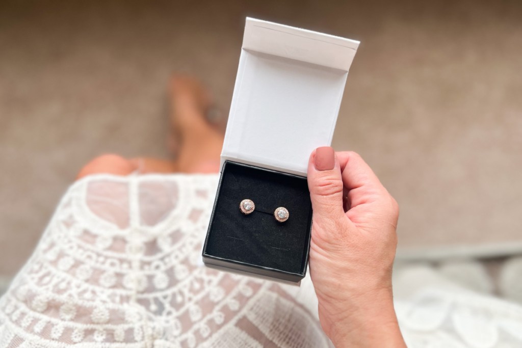hand holding box of earrings over white dress