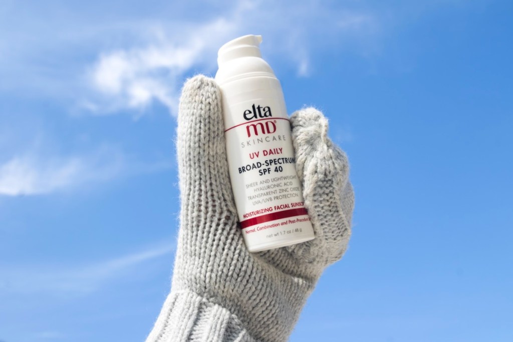 hand wearing mitten holding up sunscreen to sky