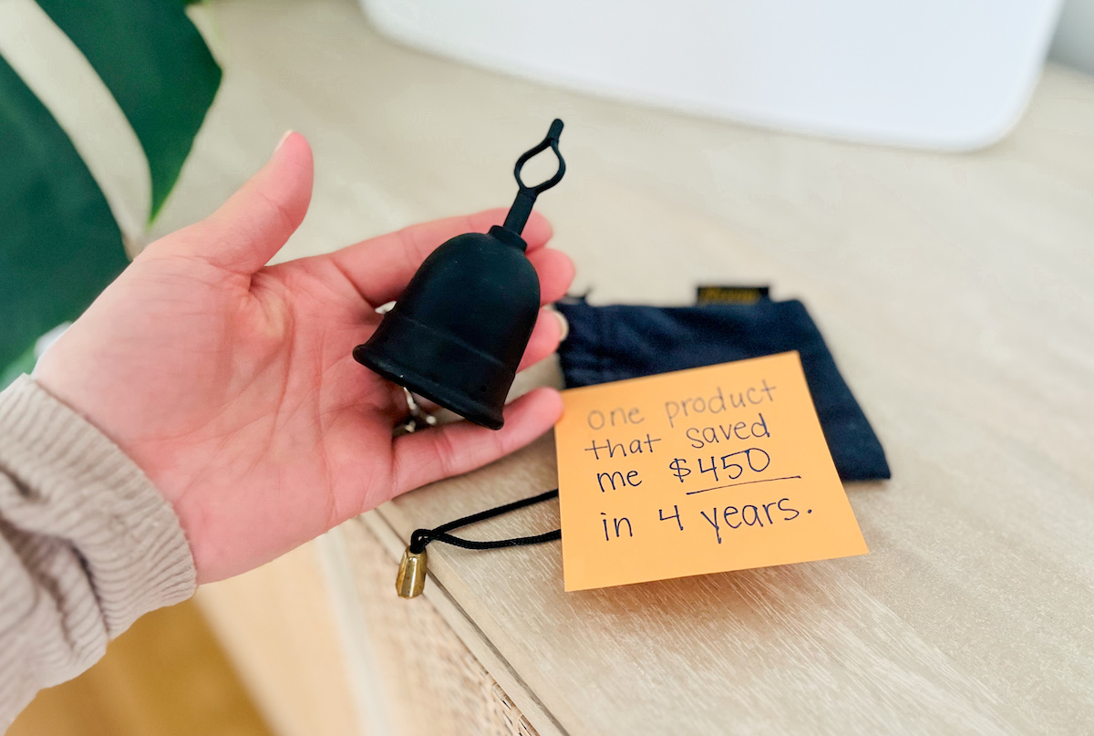 Hand holding black menstrual cup next to savings post it note 