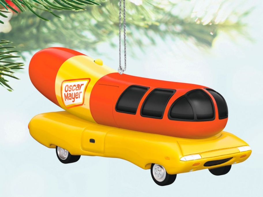 an Oscar Mayer Wienermobile Christmas ornament hanging from a tree limb