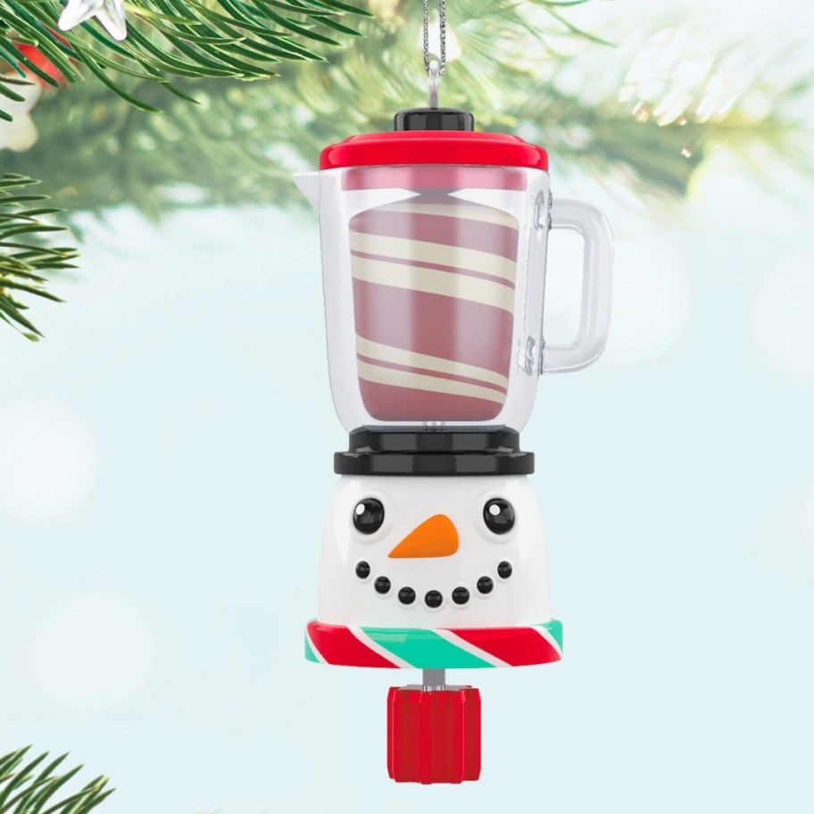 a snowman head with a blender above it with a peppermint swirling inside Christmas ornament hanging from a tree limb