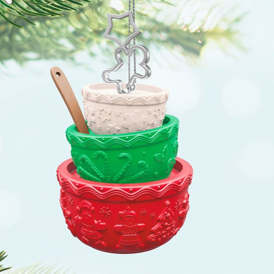 a set of 3 mixing bowls in red, green, and white with a mini spatula and gingerbread shaped cookie cutter Christmas ornament hanging from a tree limb