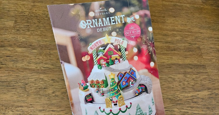 hand holding a Hallmark Christmas Ornament Debut Book, wood table behind it
