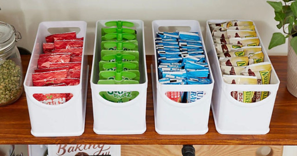 four white idesign bins with snacks in them on shelf