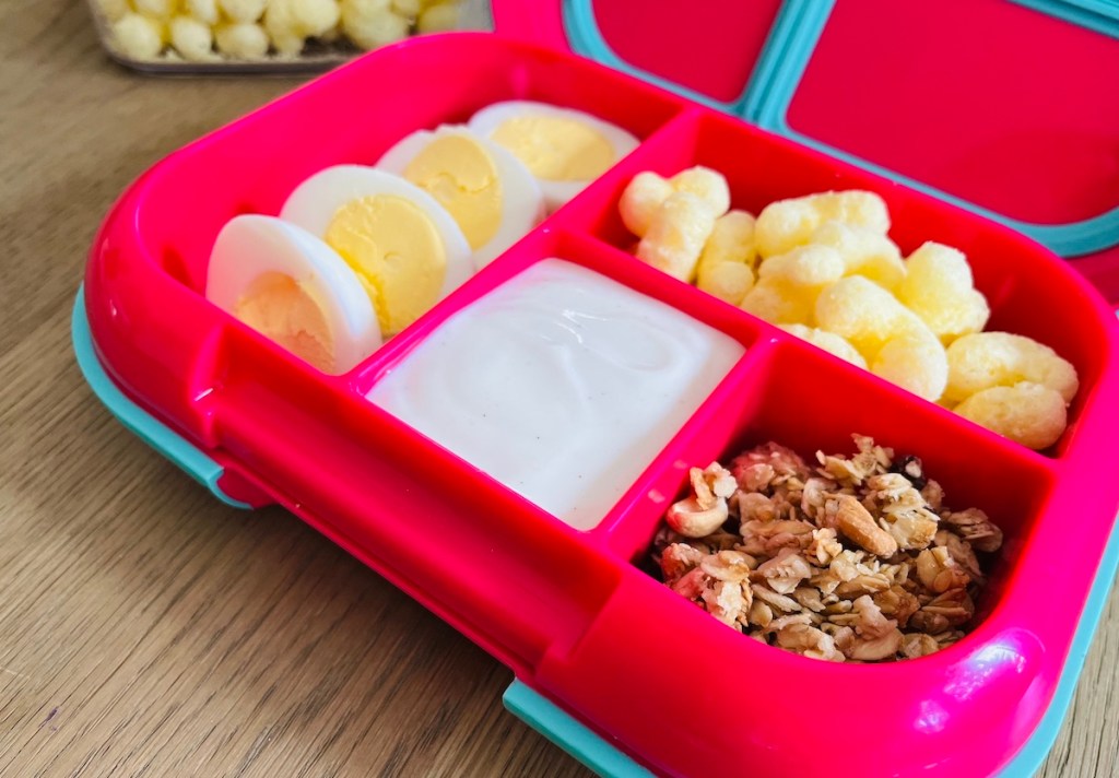 close up of bentgo style lunch box on wood table with yogurt eggs and nuts - kids lunch ideas