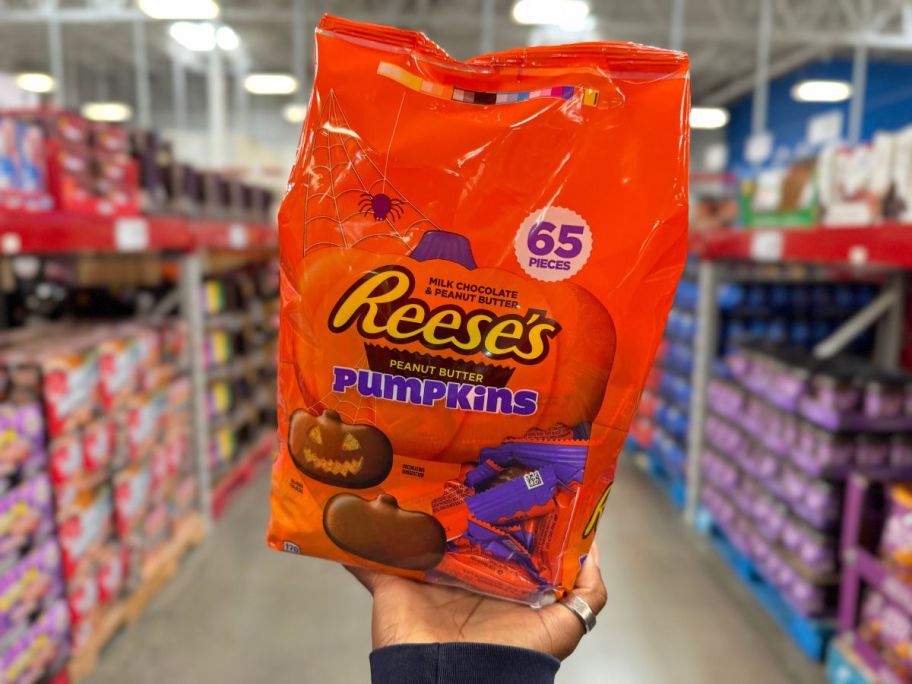 a womans hand holding a 65 count bag of reeses pumpkins