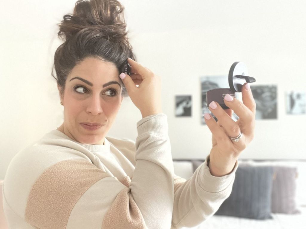 Woman with dark brown hair up in bun using Style Edit Root Touch Up Powder to cover gray roots