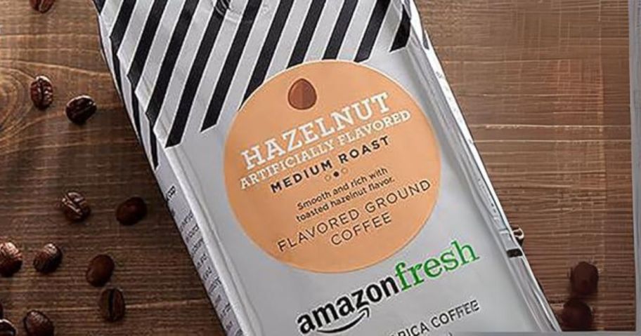 AmazonFresh Hazelnut Flavored Ground Coffee 12oz Bag laying down next to coffee beans