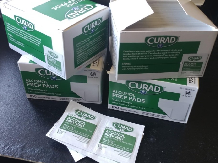 4 green and white boxes of Curad Thick Alcohol Prep Pads with a couple individual pads in packets in front of the boxes