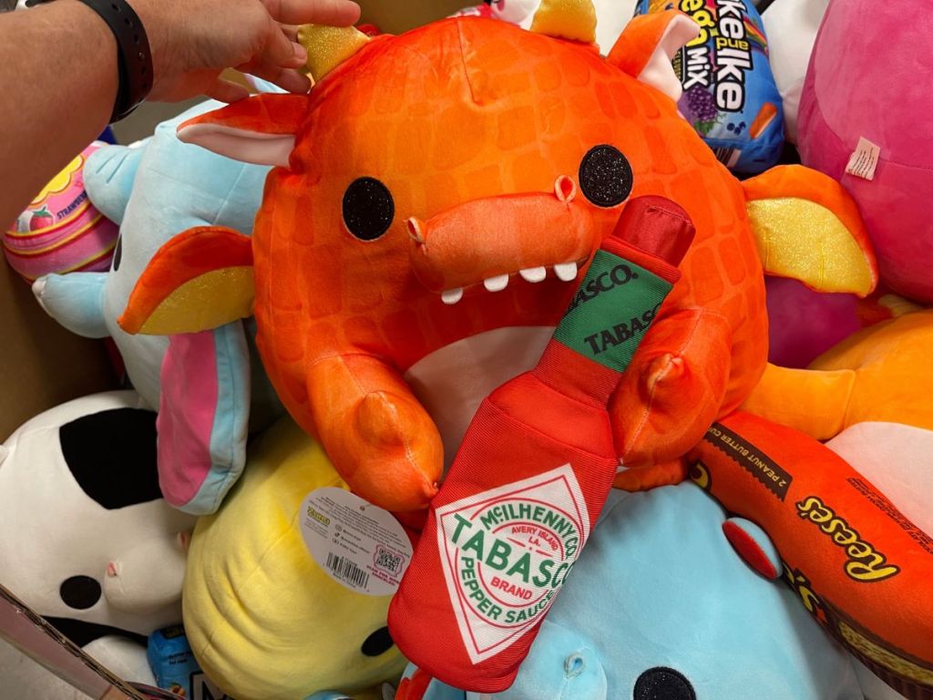 A dragon plush toy holding a bottle of tobasco 