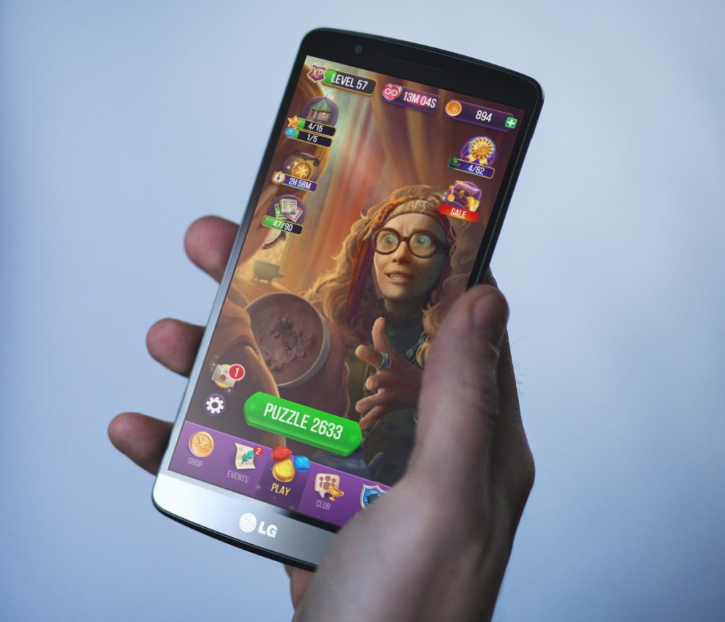 Hand holding a phone with Harry Potter: Puzzles & Spells game shown on the screen