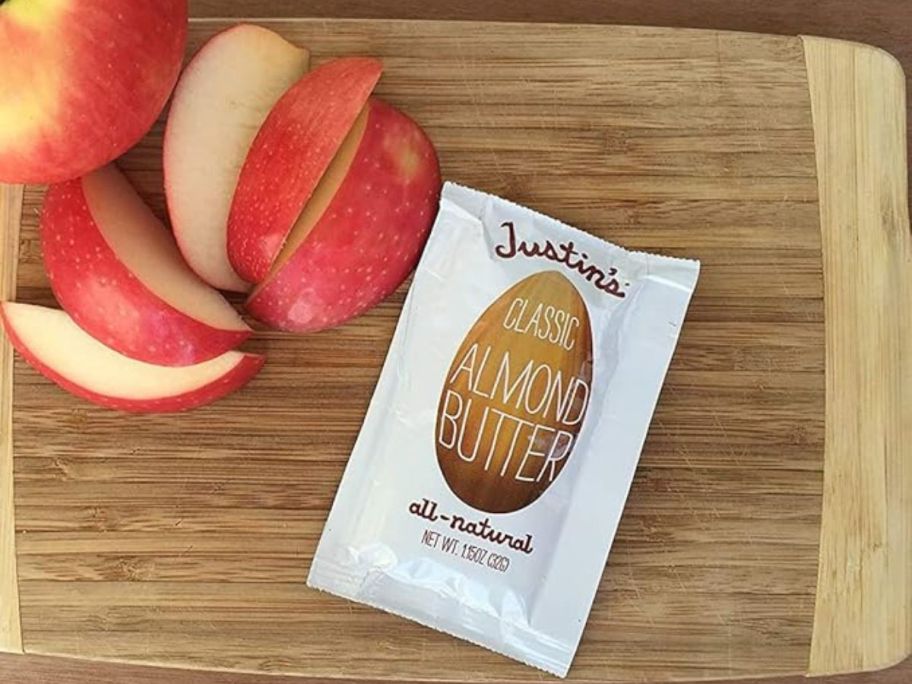 A pouch of Justin;'s Almond Butter on a cutting board next to apple slices