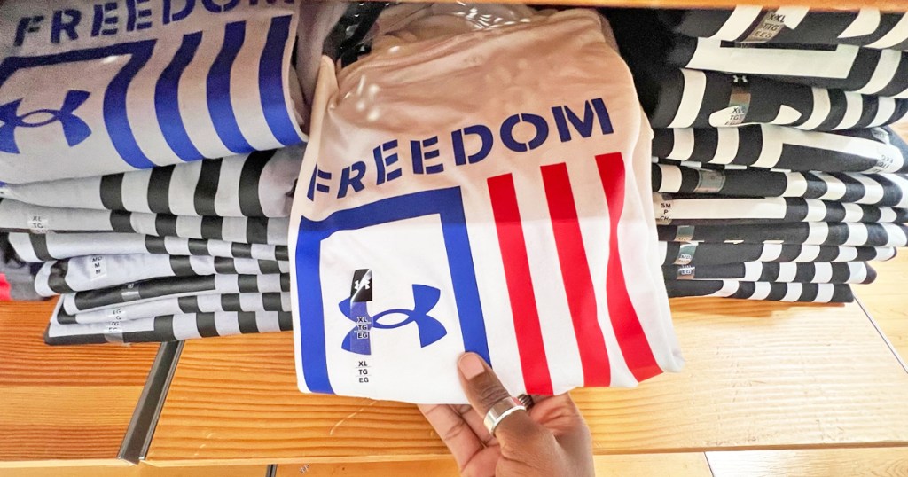 hand grabbing an under armour flag tee from store display shelf