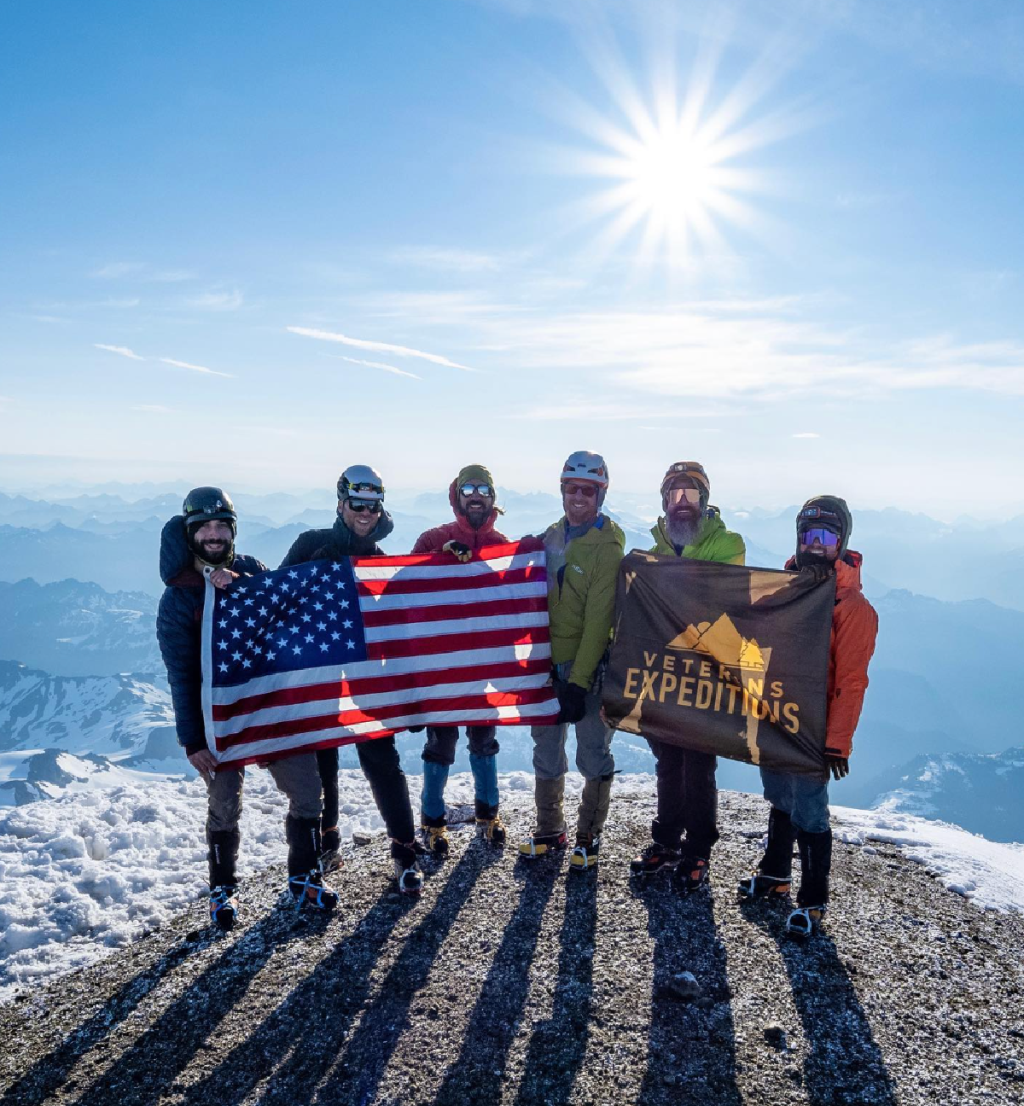 Veterans on a mountain summit holding up a sign