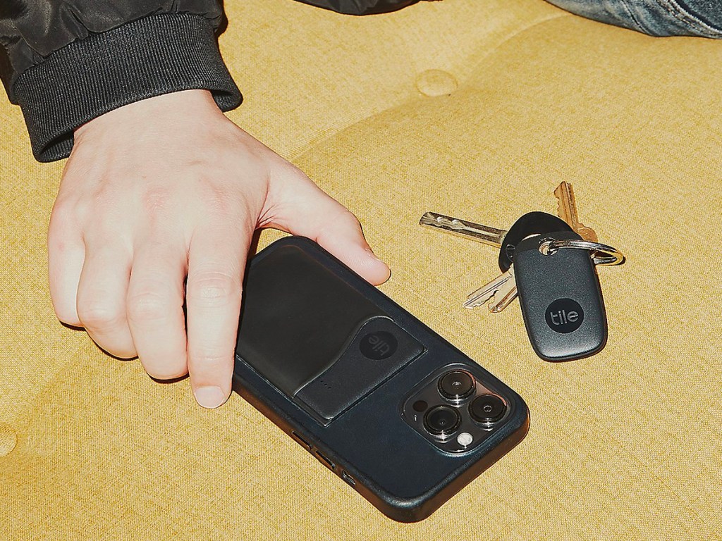 hand holding black phone with tile on it next to keys 